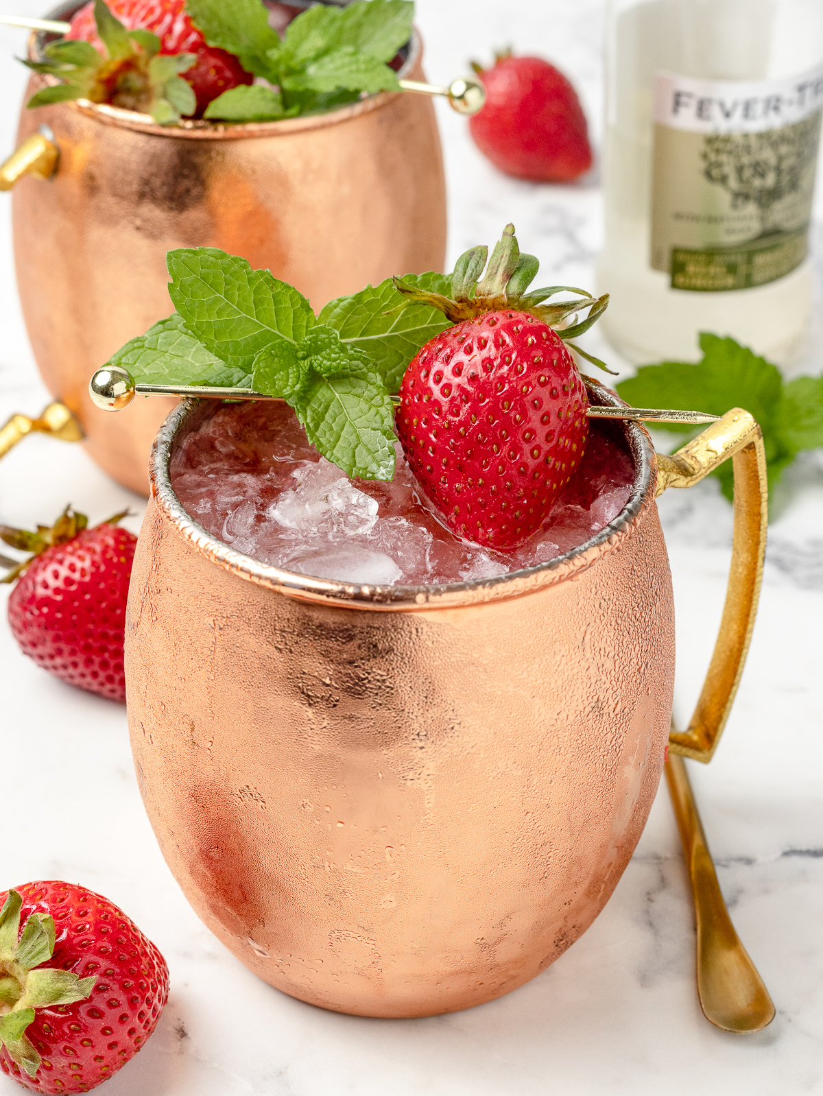 Close up of the strawberry mocktail garnish. You can see a whole fresh strawberry and mint leaves sitting overtop the copper mug.