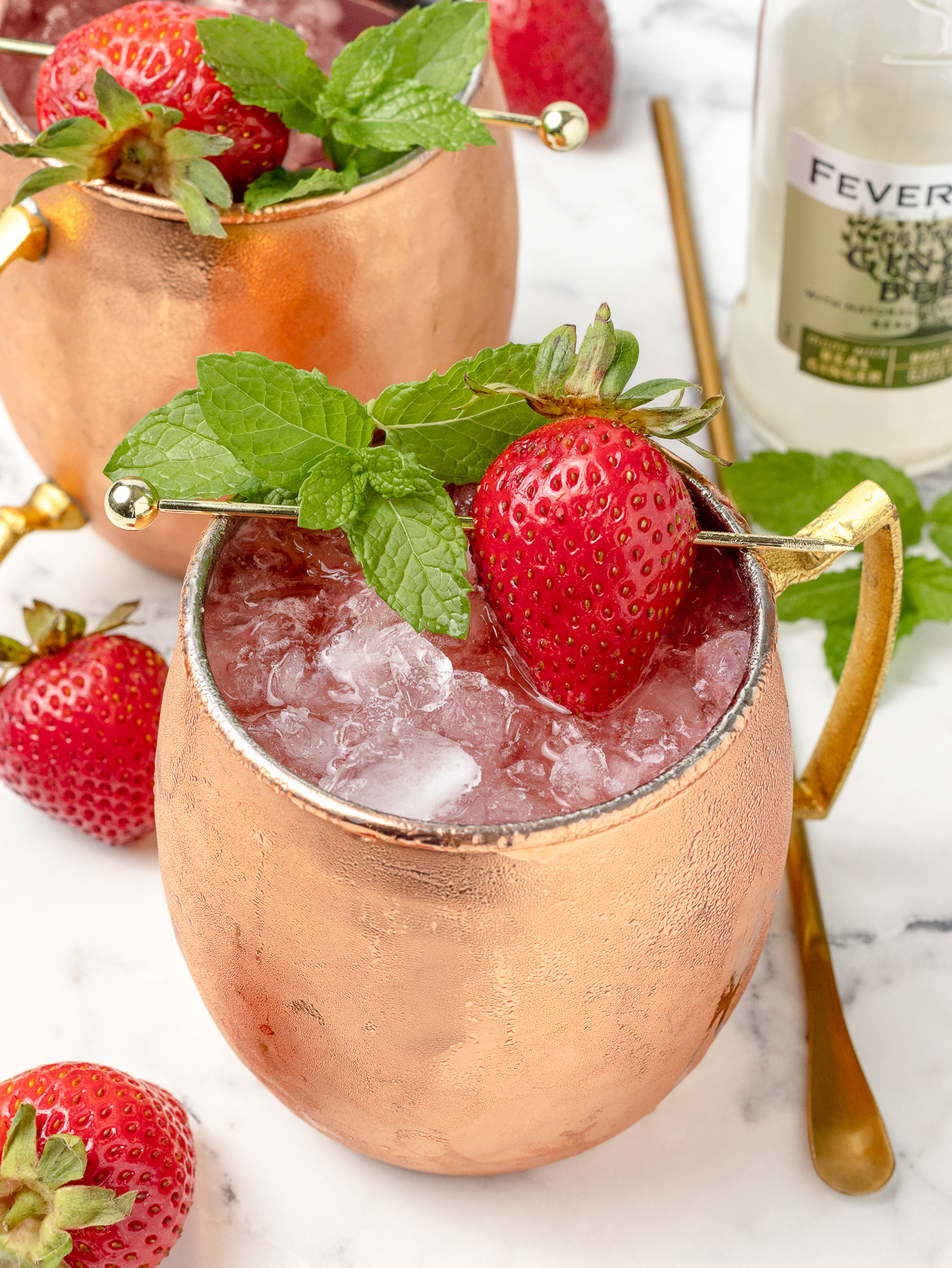 2 mocktails in copper mugs. There are made with fresh strawberries, lime juice, honey, ginger beer, and club soda.