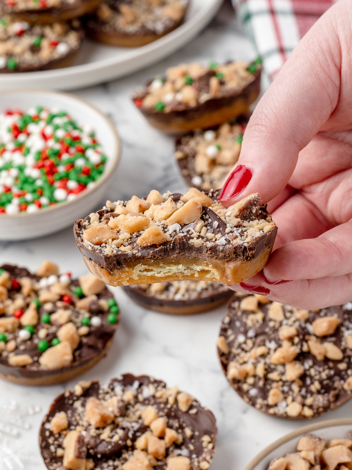 Hand holding a Christmas Crack Cookie with a bite taken from it. There are more in the background.