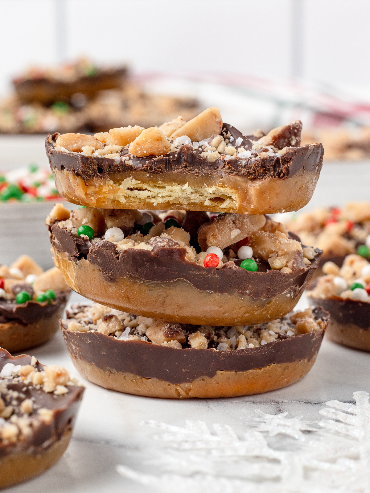 Stack of Christmas Crack Cookies. The top one has a bite taken from it so you can see the layers of cracker, toffee, and chocolate.