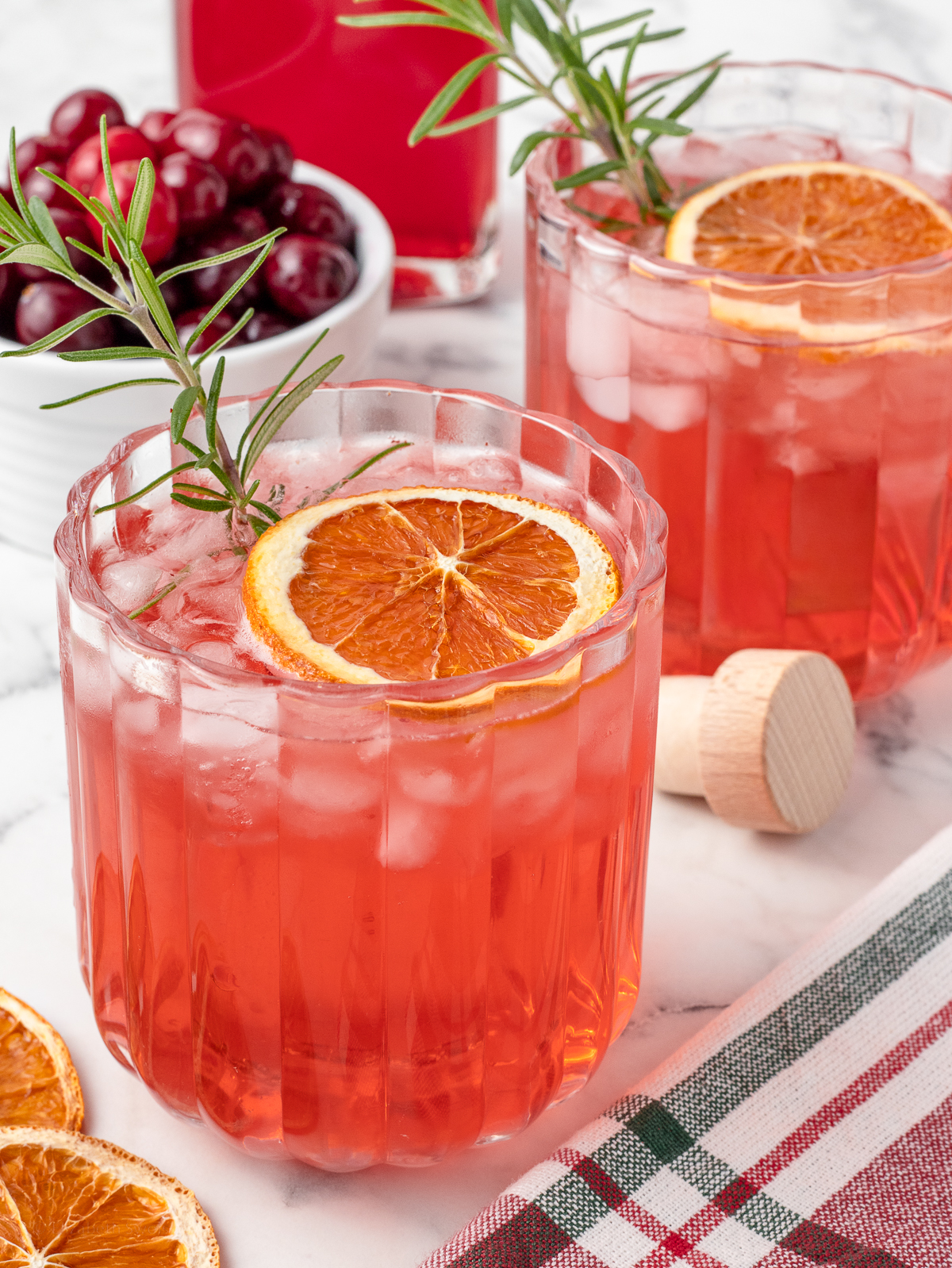 Two shrub drinks with a bowl of fresh cranberries in the background.