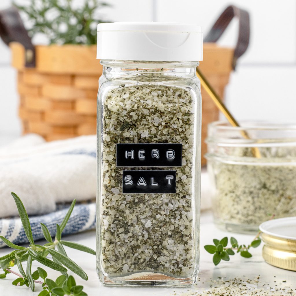 Herb Salt in a shaker jar with fresh herbs surrounding it.