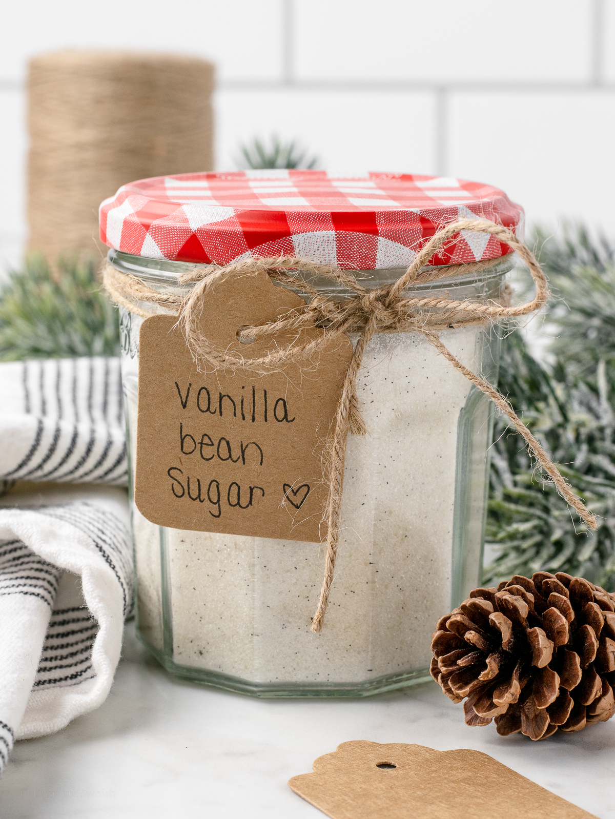 Jar of the sugar with a pretty bow and label that reads "Vanilla Bean Sugar." It is ready for gifting to friends and family.