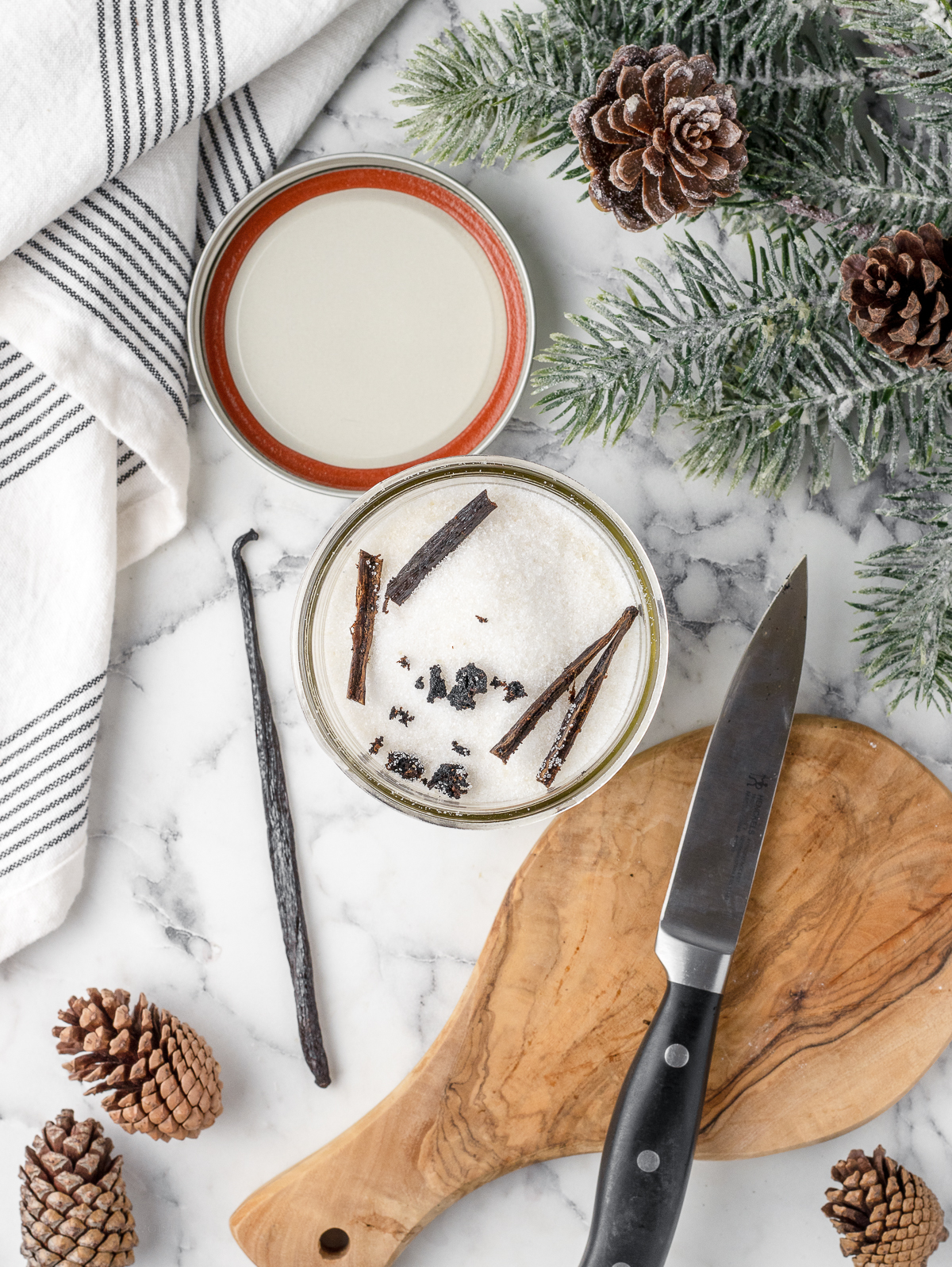 Jar filled with granulated sugar, vanilla seeds, and empty vanilla bean pods. It's ready to shake together.