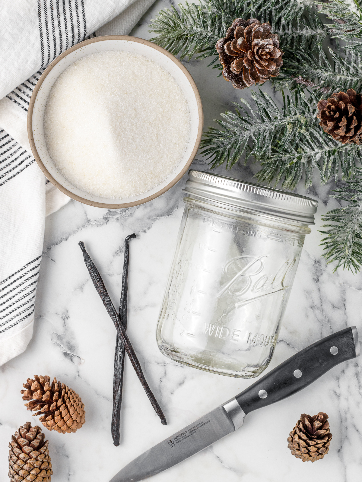 Granulated sugar and 2 vanilla beans. There is also a knife and a jar with an airtight lid.