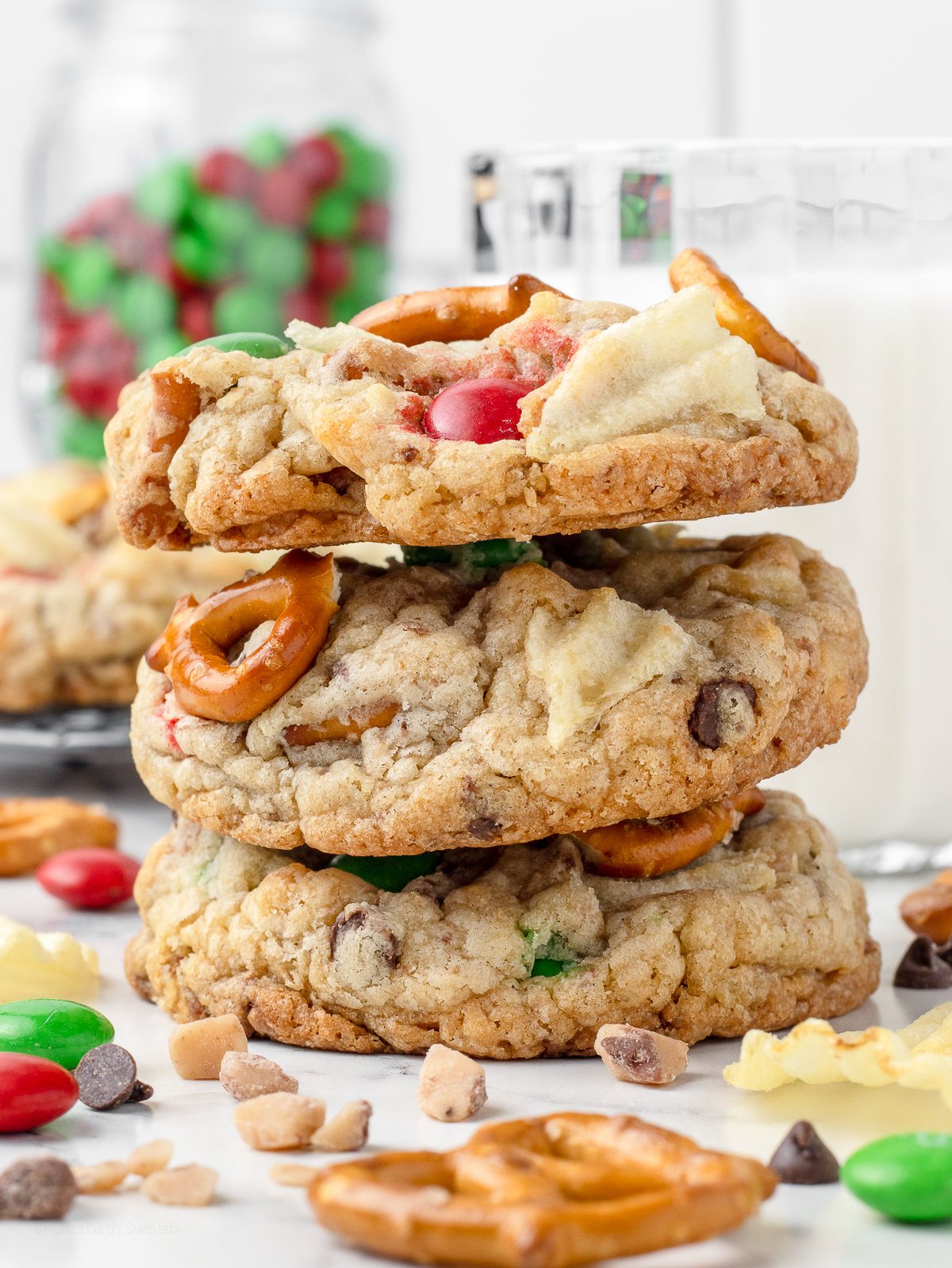 Stack of three cookies with a glass of milk. There are more cookies in the background.