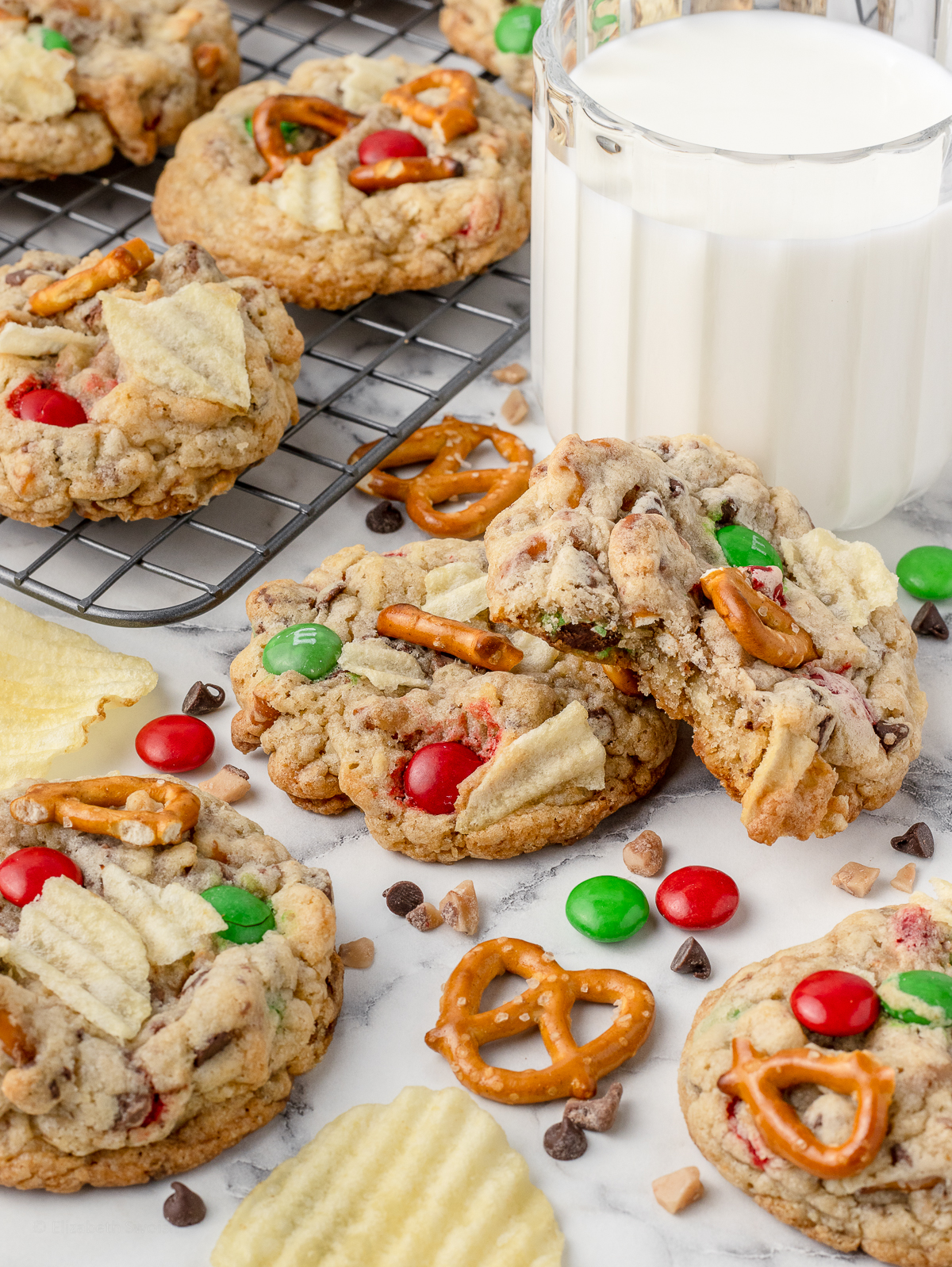 Christmas Kitchen Sink Cookies on the counter with a glass of milk and more on a cooling rack.
