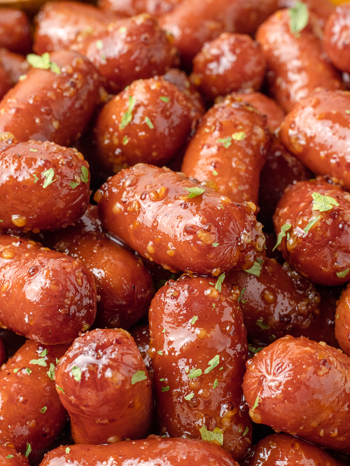 Close up of the sausages to see a sticky honey mustard sauce and parsley flakes. The sausages are plump, juicy, and perfectly caramelized.
