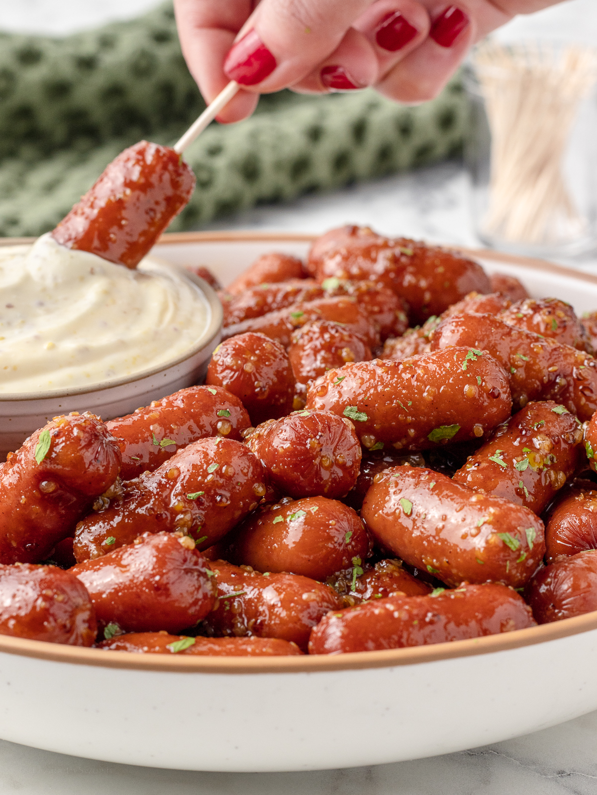 Hand dipping a honey mustard coated sausage into a mustard mayonnaise sauce.
