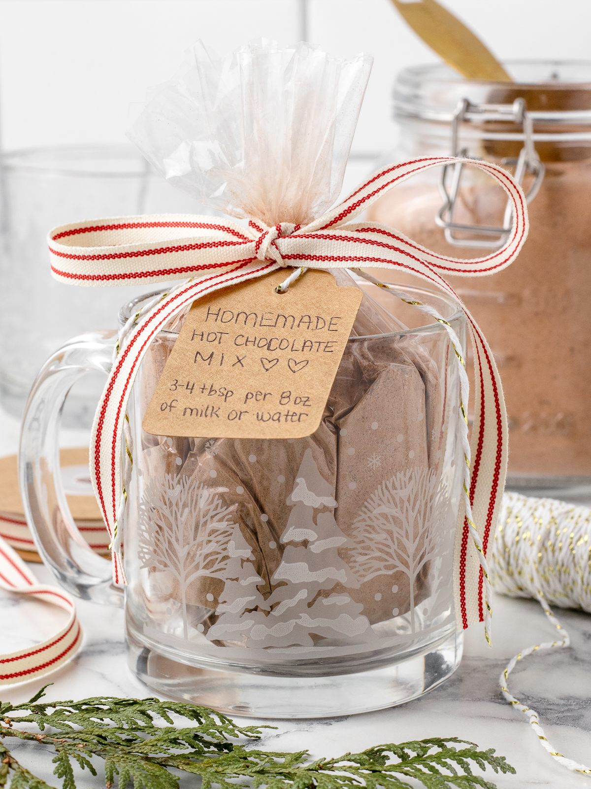 Hot Chocolate Mix given as a gift. It is in a clear baggie that is tied off with a bow and gift tag. It is sitting in a Christmas mug.