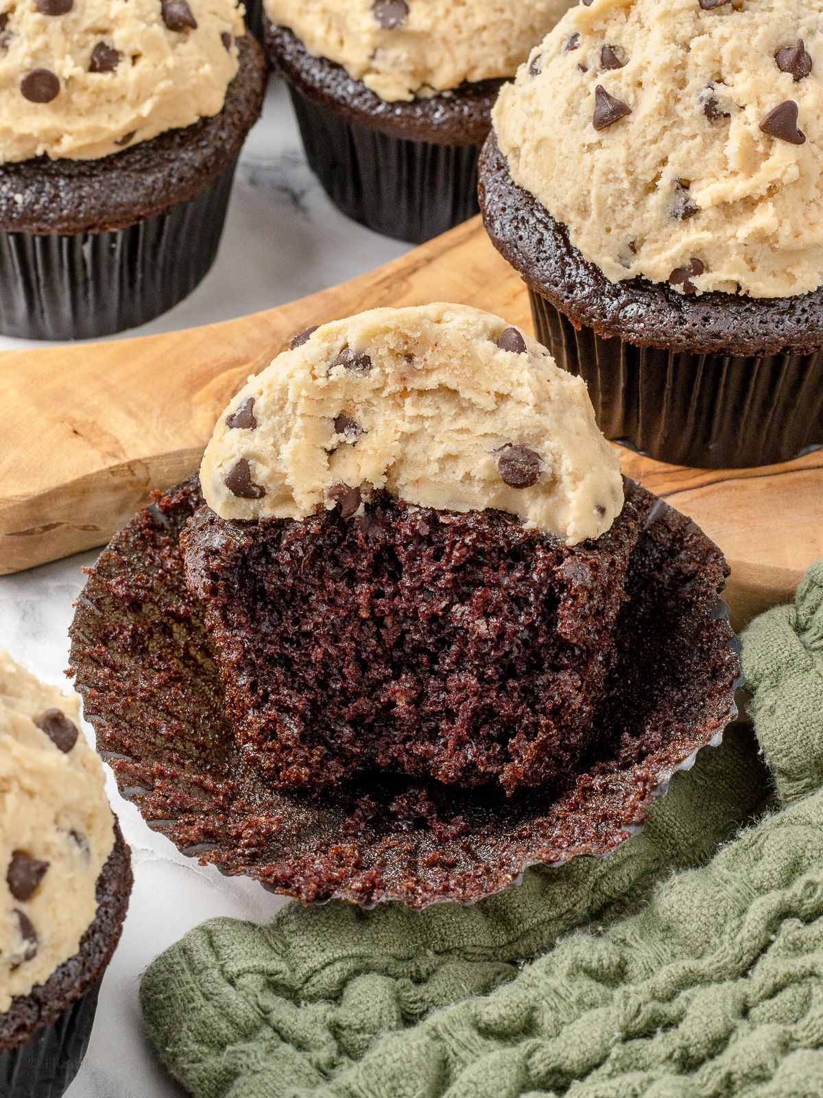 Bite taken from cupcake to see a soft chocolate cupcake and a thick layer of chocolate chip cookie dough frosting.