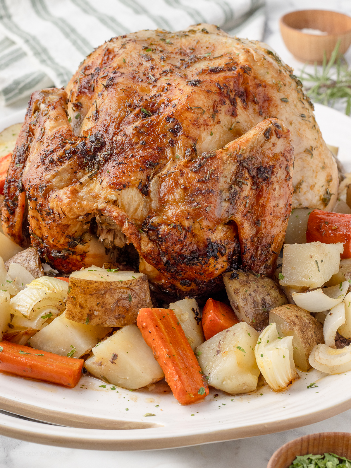 Crispy and golden brown Herb Roasted Chicken resting upon roasted potatoes, carrots, and onions. It's ready to cut and serve for dinner.