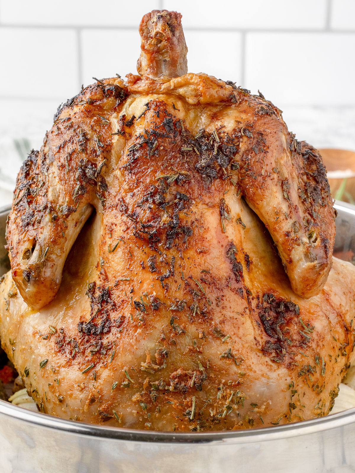 Close up of the roasted chicken to see it's crispy and golden brown skin. There are speckles of herbs like rosemary, thyme, and parsley.