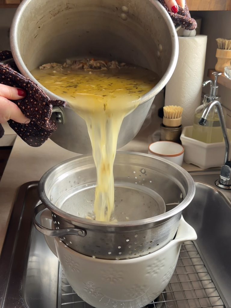 Stock being poured over a fine-mesh strainer and colander to be separated from the bones and pulp.