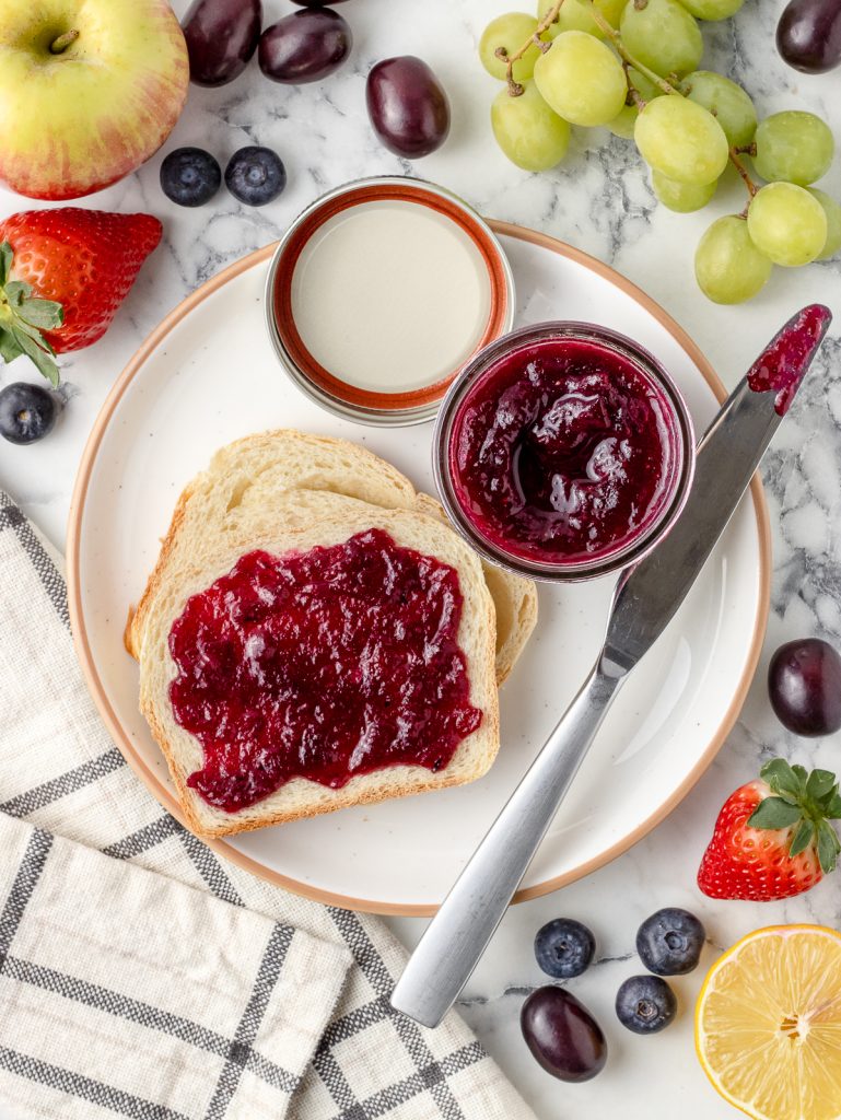 Plate with a jar of jam plus two slices of homemade sandwich bread. One is slathered with the Mixed Fruit Jam.