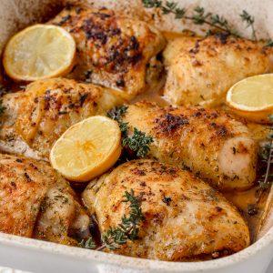 Six baked Lemon Chicken Thighs with roasted lemons and thyme. Ready for serving and eating.