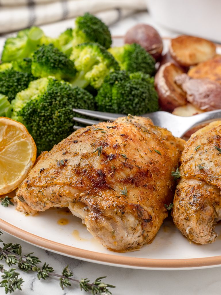 Plate of baked Lemon Chicken Thighs with steamed broccoli and roasted potatoes ready to eat.