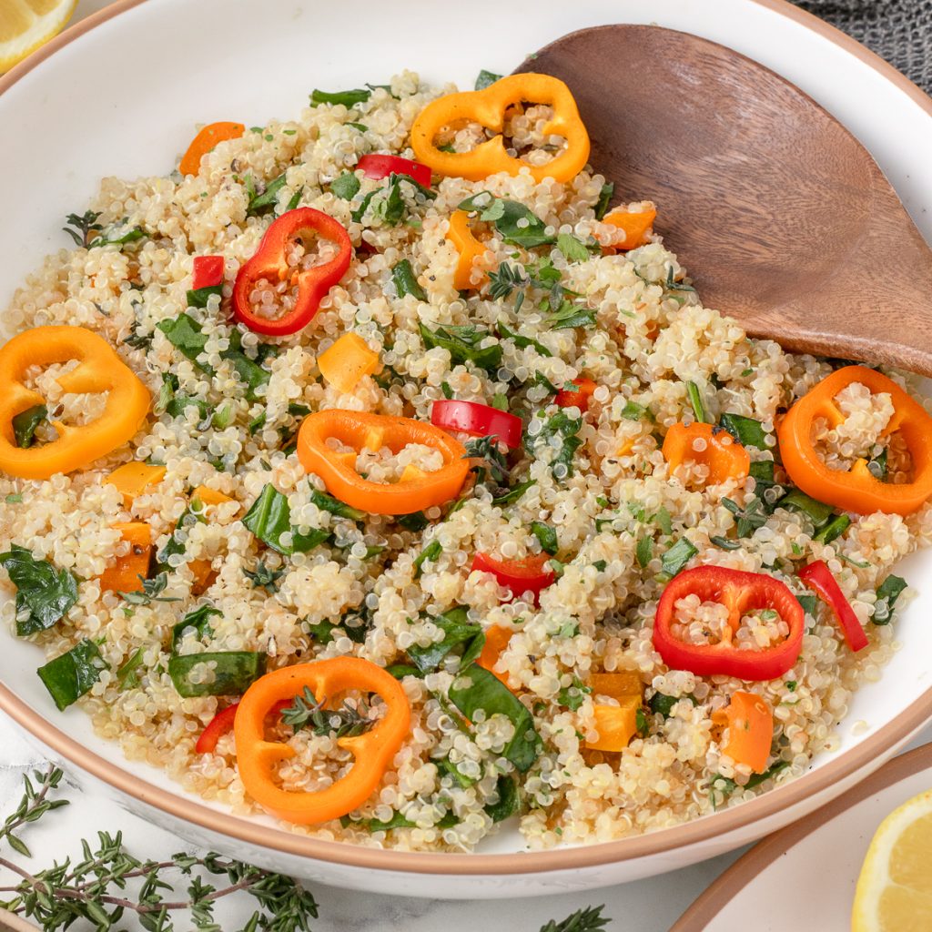 Bowl of Warm Quinoa Salad with spinach, herbs, and sweet bell peppers that are red, yellow, and orange.