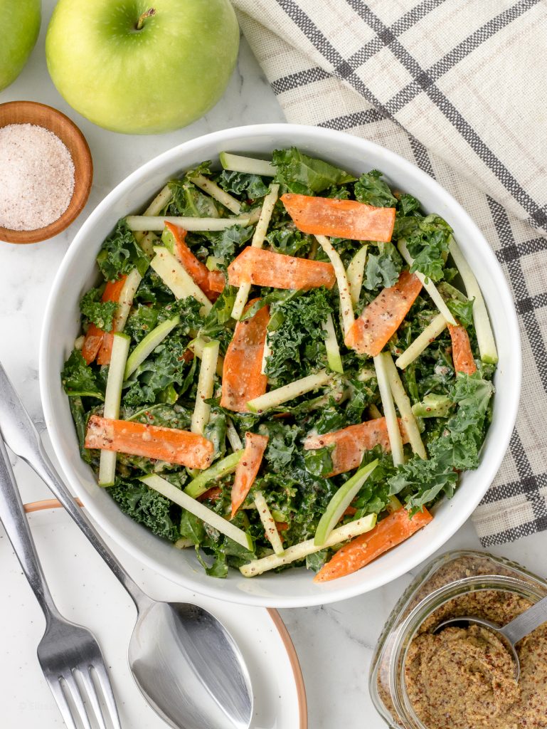 Overhead image of the slaw. You can see how bright and vibrant it is with kale, carrots, and green apples. There's salt, more green apple, and stone ground mustard on the side.