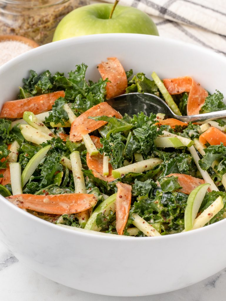 A big bowl of the slaw. You can see the crunchy kale, matchstick green apples, and ribbons of carrots dressed in a honey mustard dressing.