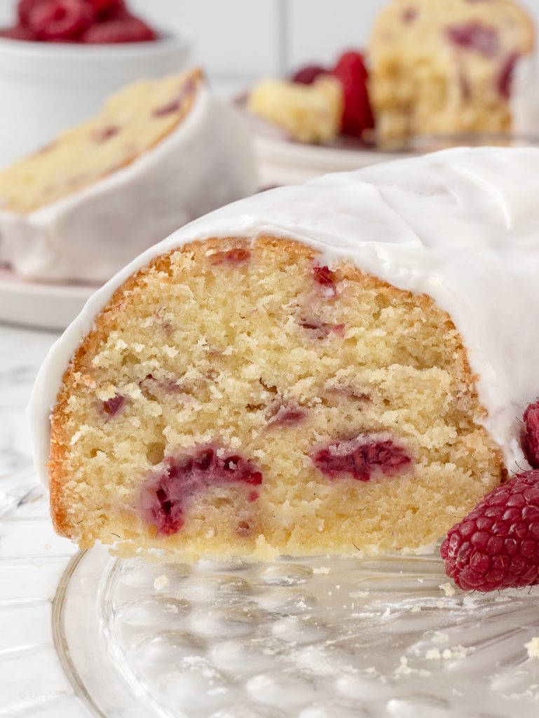 Slices removed from the bundt cake. They are on plates in the background. with fresh raspberries.