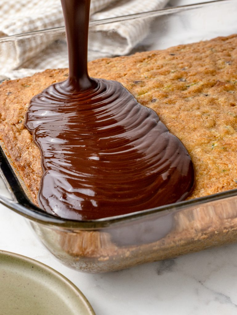 Pouring the chocolate ganache frosting over top of the cooled cake.