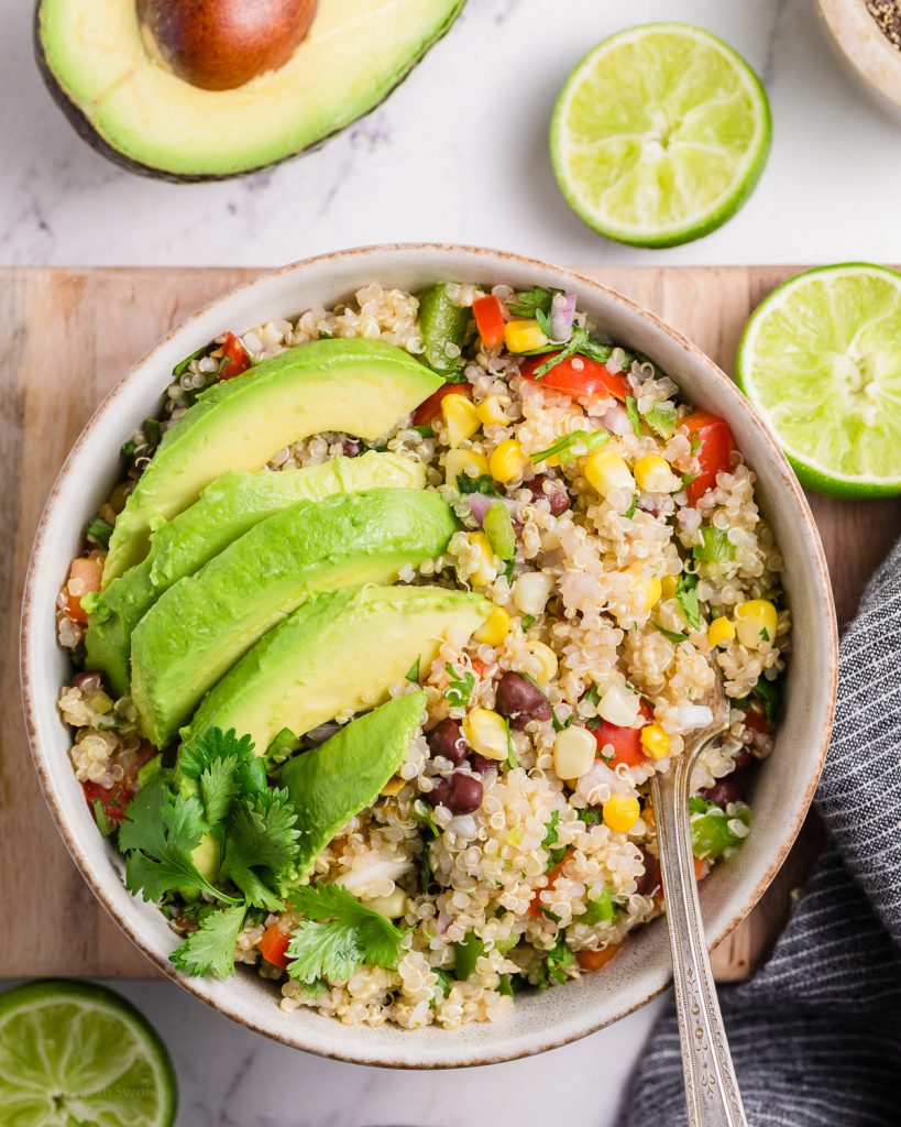 Bowl of Mexican Quinoa Salad topped with avocado and fresh cilantro. There is a fork in the bowl ready to eat.