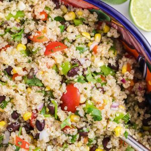 Close up of the Mexican Quinoa Salad so you can see the tomatoes, green peppers, red peppers, corn, black beans, red onion, and fresh cilantro. There are limes on the side to represent the lime dressing.