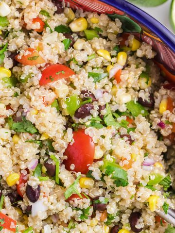 Close up of the Mexican Quinoa Salad so you can see the tomatoes, green peppers, red peppers, corn, black beans, red onion, and fresh cilantro. There are limes on the side to represent the lime dressing.