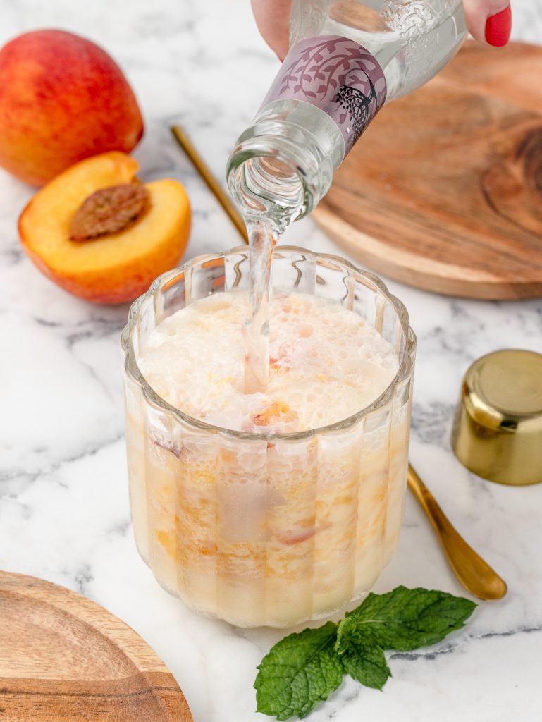Pouring the club soda overtop of the muddled peach syrup and half and half.