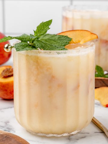 Glass of Peaches and Cream Mocktail garnished with a fresh peach and mint leaves.